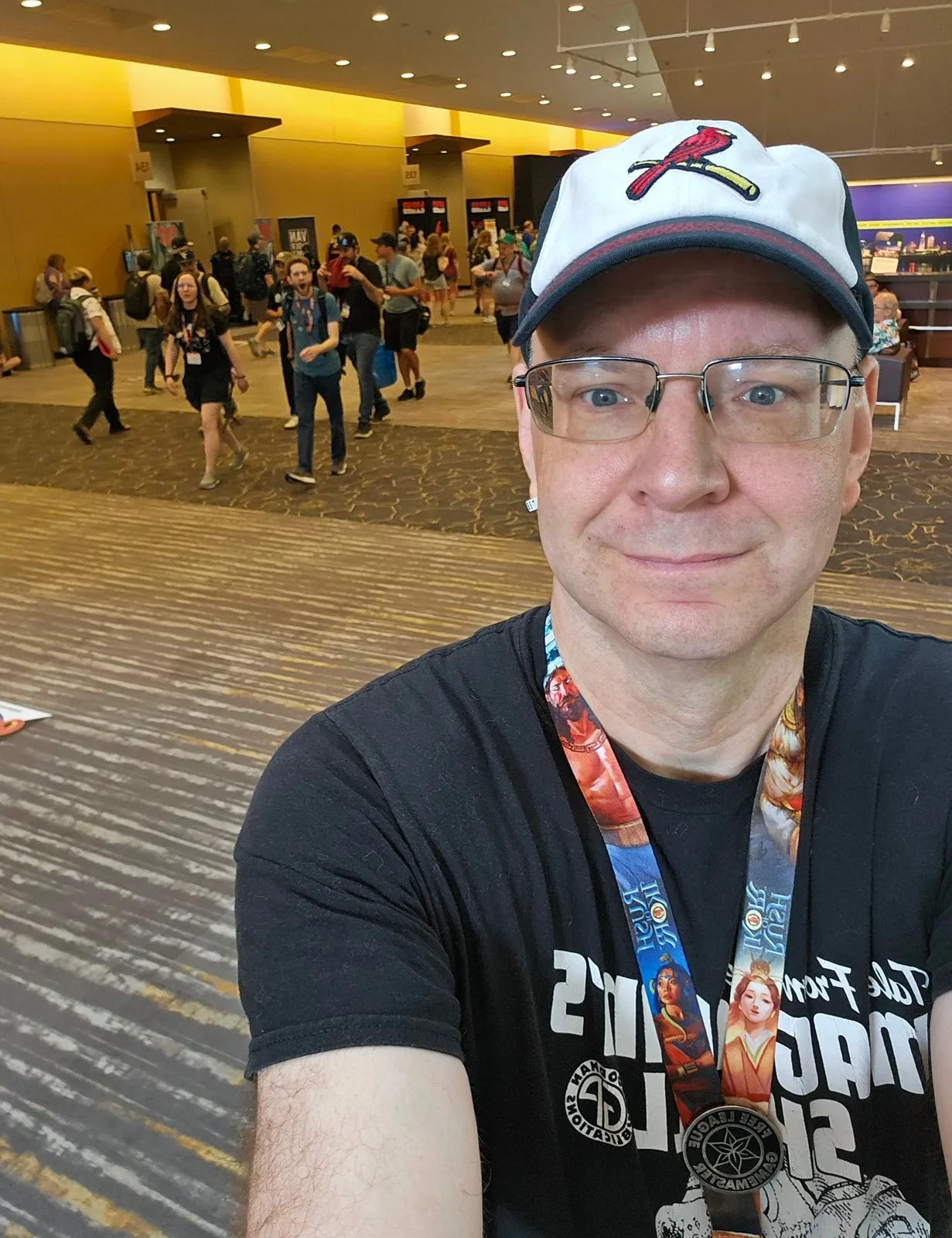 Bryant smiling in a convention hallway, wearing a Gamemaster medal and Free League lanyard, con-goers passing in the background.