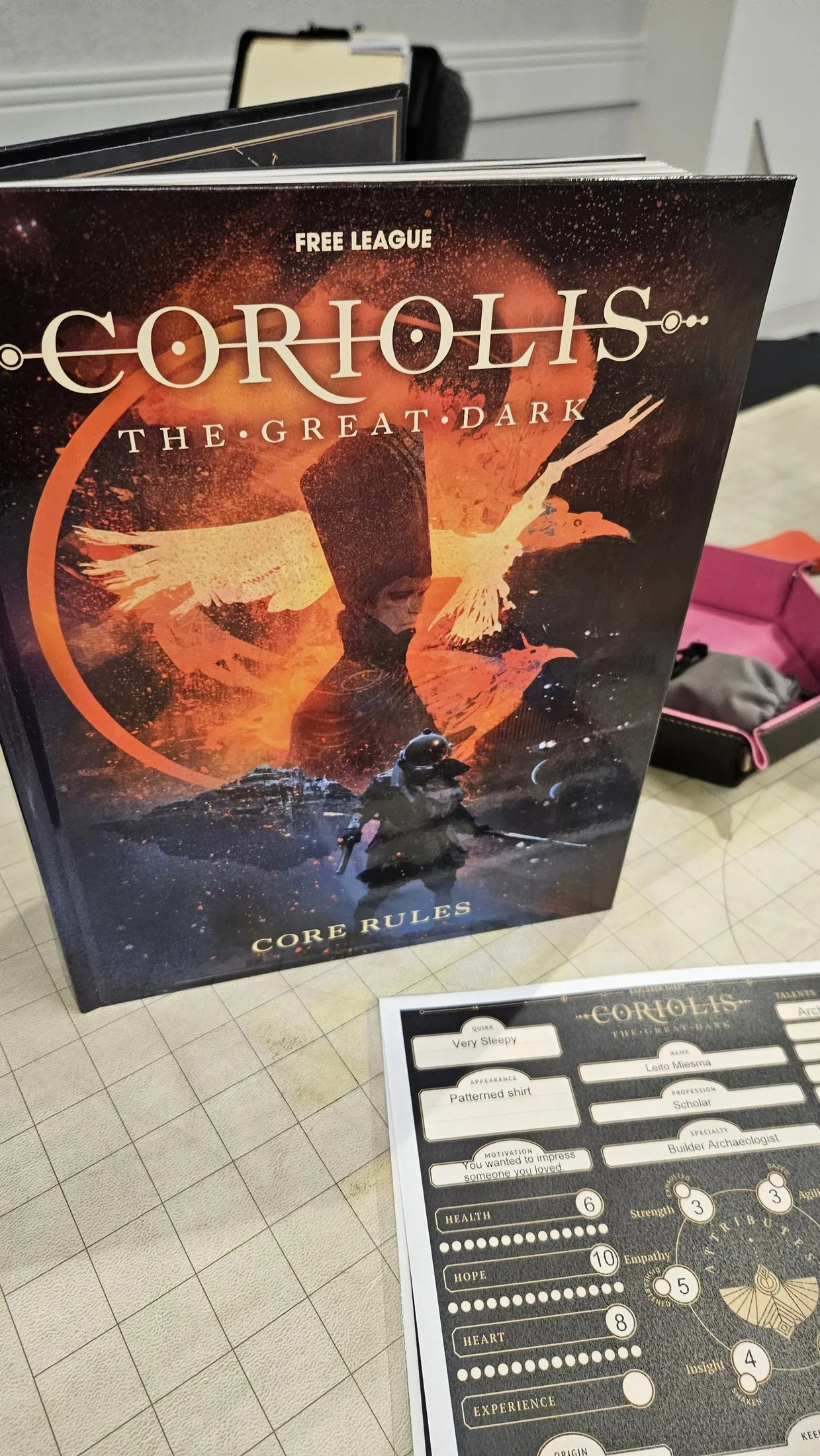 The Coriolis: The Great Dark Core Rules book standing upright on a game table, with a filled-out explorer sheet for a Scholar character in front of it.
