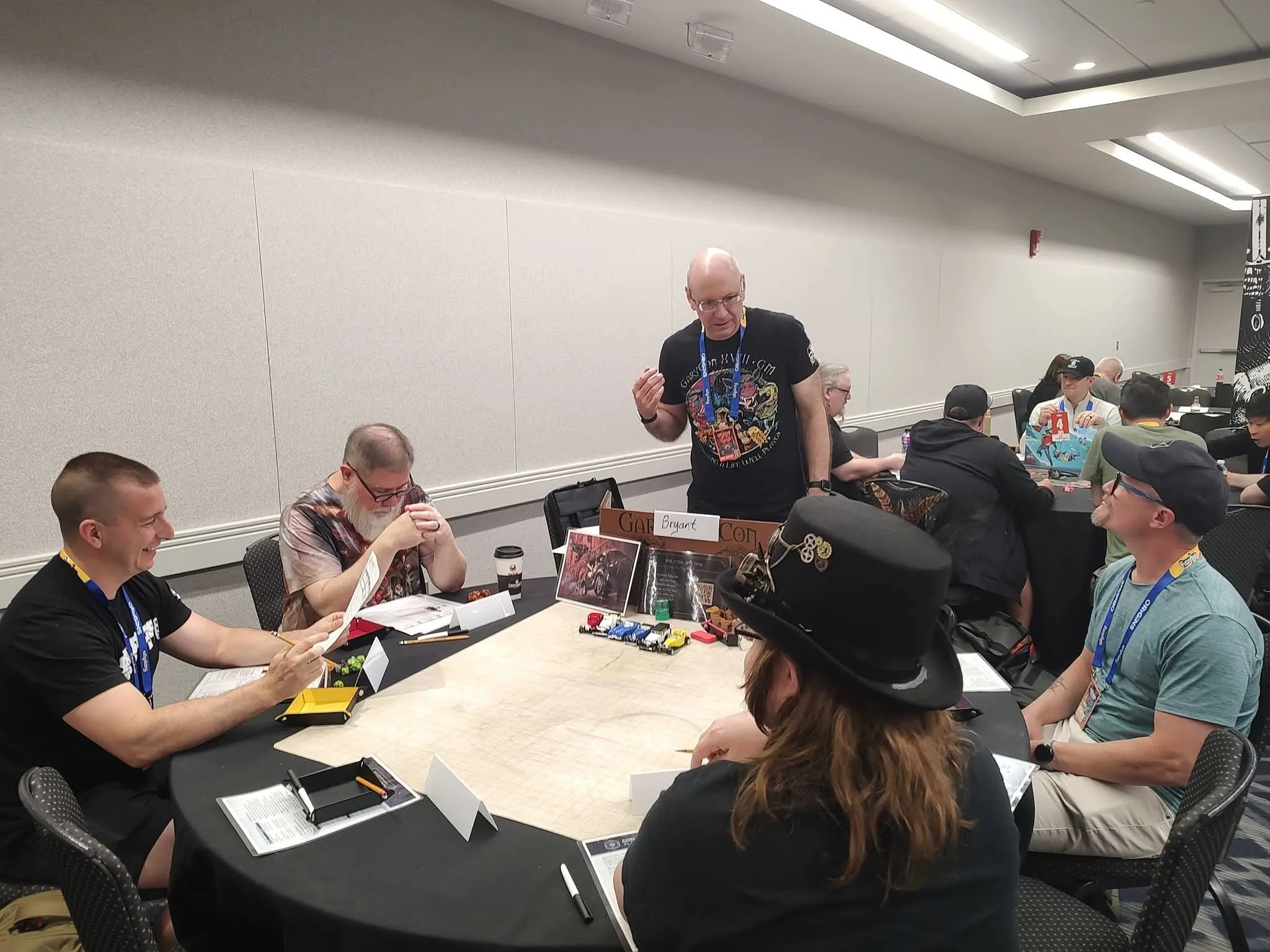 Bryant running Pedal to the Metals at Origins 2026, standing at the table while players lean in around a city map with toy race cars